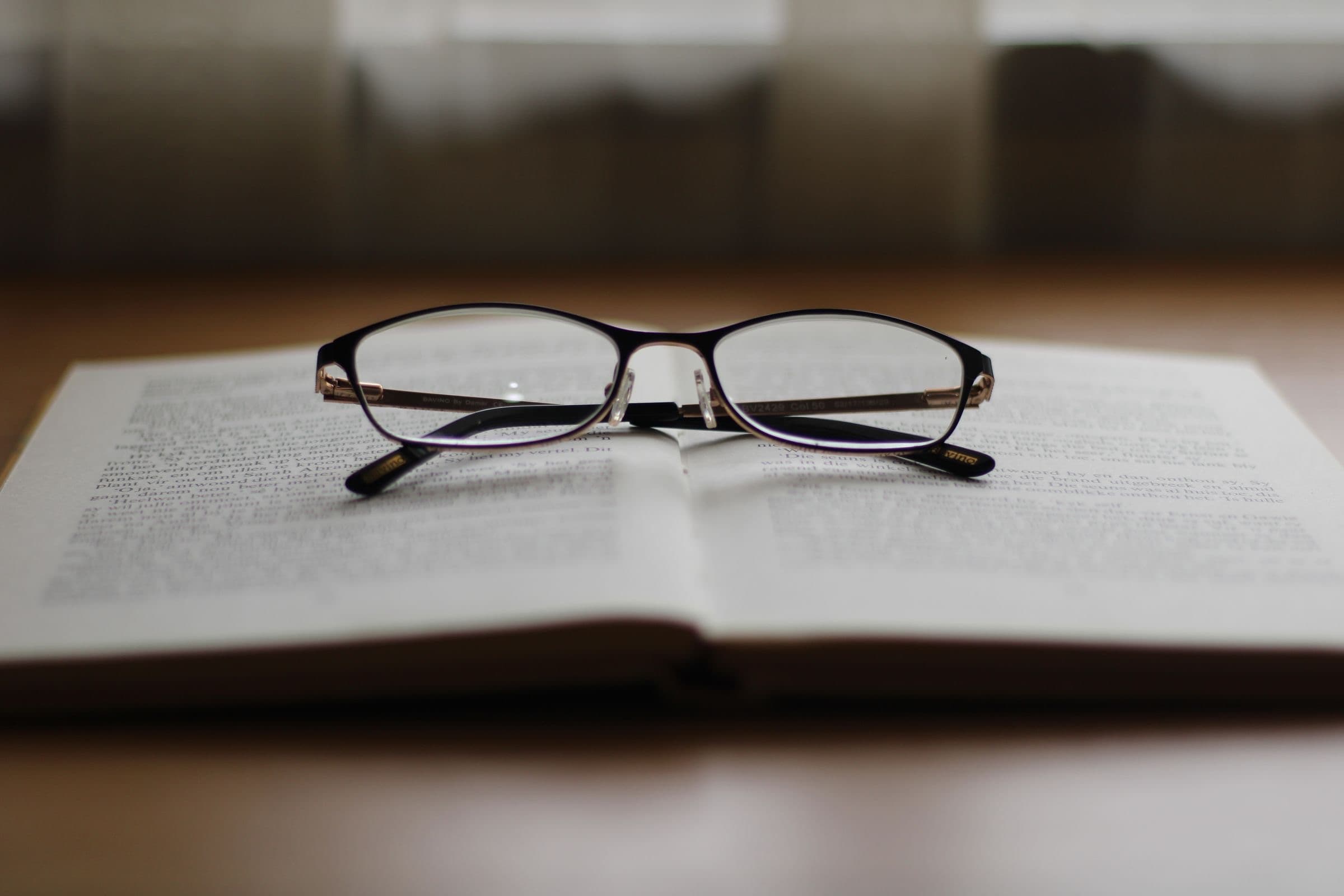 Reading glasses resting on an open book on a wooden table